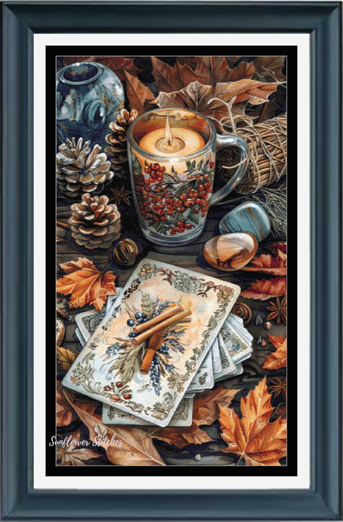 A framed still life artwork featuring a lit candle in a glass mug filled with red berries, surrounded by autumn leaves, pinecones, a blue vase, and a stack of illustrated cards on a dark tabletop. The piece is presented in a dark teal frame with a white mat.