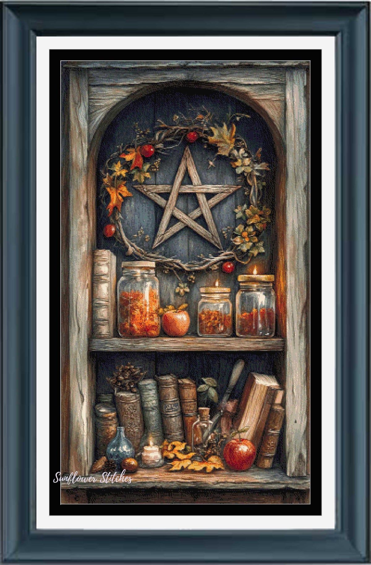 Framed cross stitch featuring a rustic autumn shelf scene with a large wooden star wreath, glass jars, books, candles, and apples, presented in a dark teal frame with white matting.
