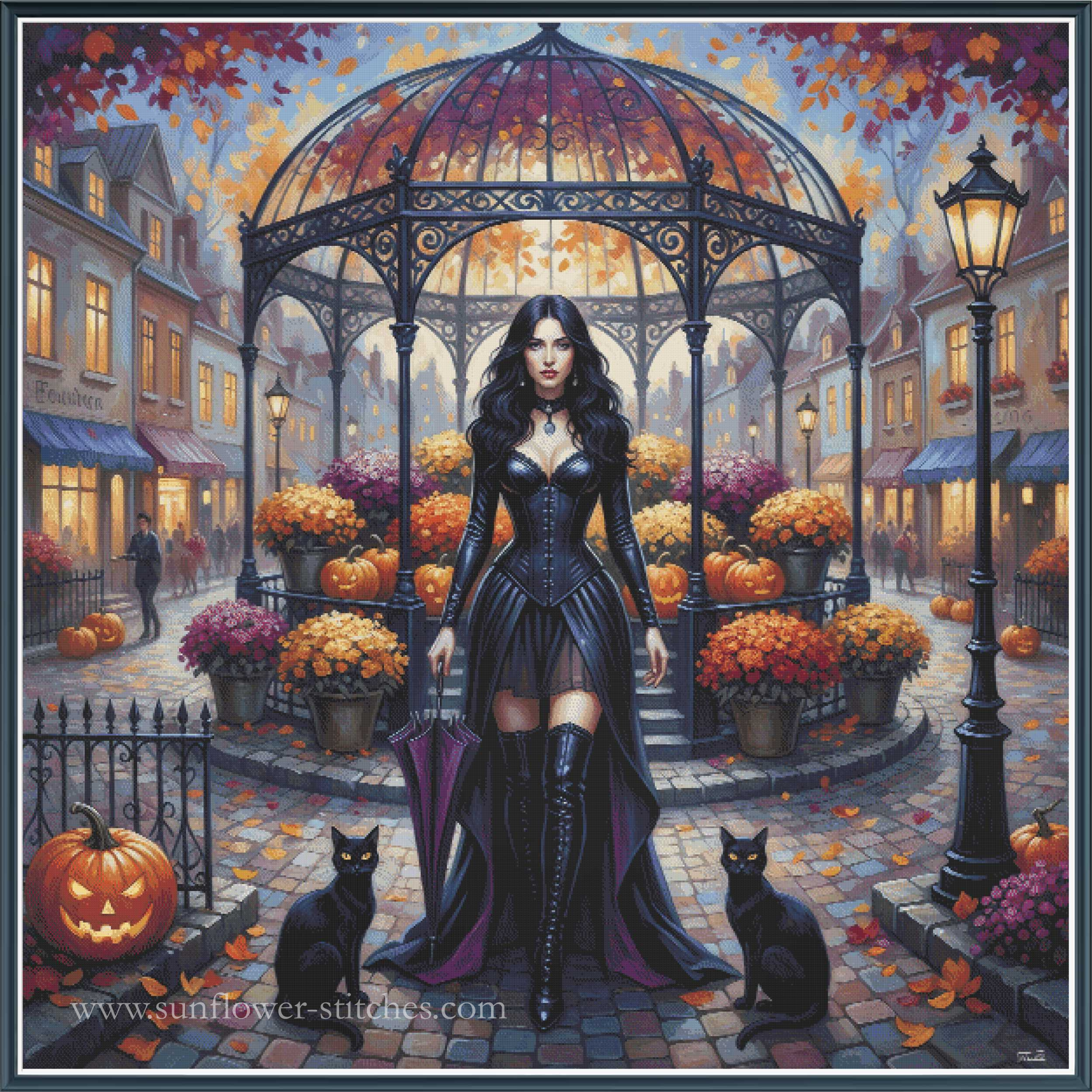 A Halloween cross stitch of a woman in a black corset and long dress standing in a cobblestone town square under a glass gazebo, surrounded by pumpkins, orange flowers, street lamps, and two black cats. 