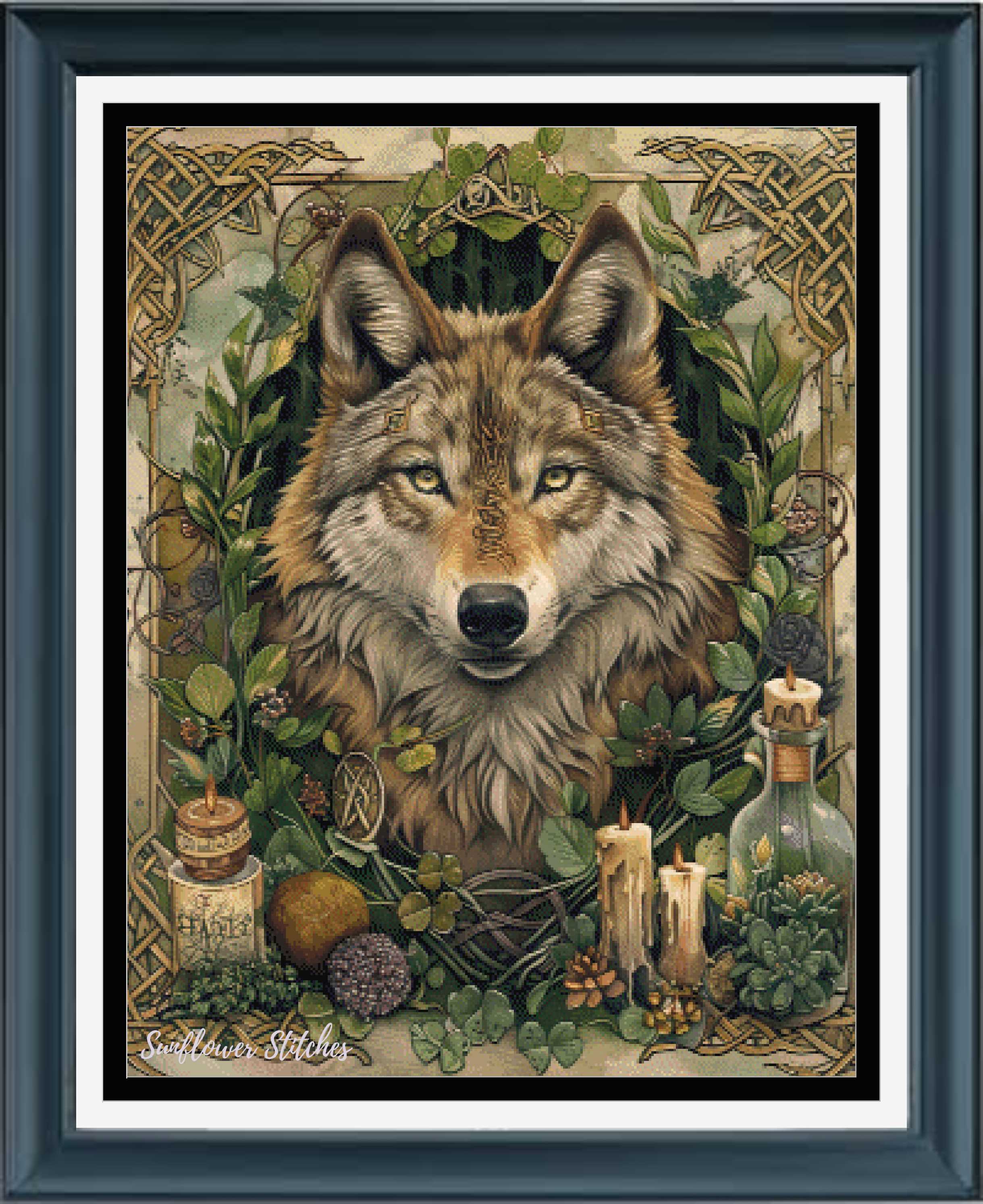 A framed cross stitch featuring a detailed illustration of a wolf surrounded by green leaves, herbs, candles, and small bottles, set within a dark frame with a white mat.