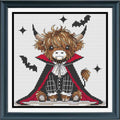 A framed cross-stitch artwork featuring a cute Highland cow dressed as a vampire, with brown fur, a black cape with red lining, white shirt details, and black bat silhouettes on a white stitched background.