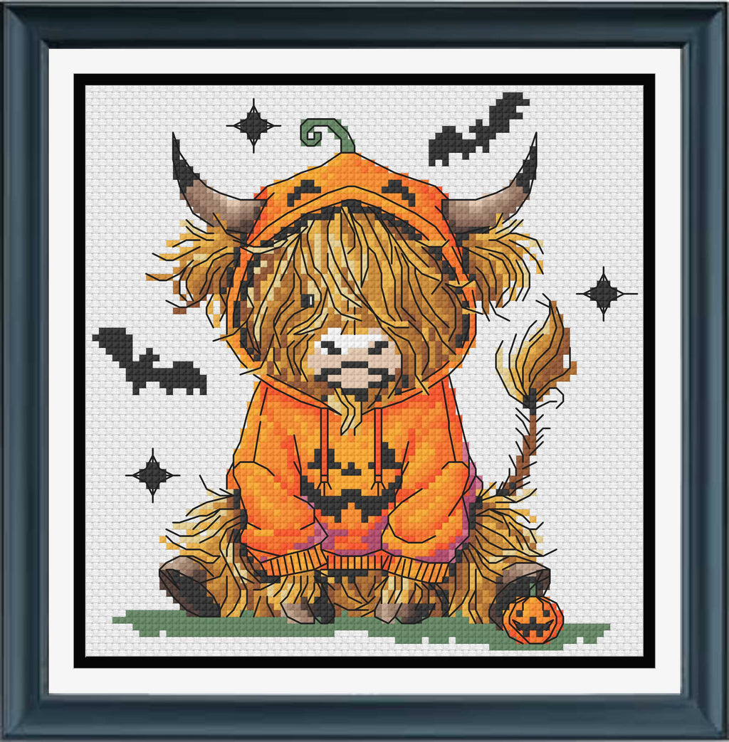 A framed cross-stitch of a fluffy Highland cow wearing an orange pumpkin costume, seated on a small patch of green grass with bats, stars, and a jack-o'-lantern around it. 