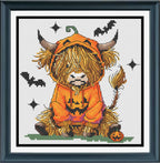 A framed cross-stitch of a fluffy Highland cow wearing an orange pumpkin costume, seated on a small patch of green grass with bats, stars, and a jack-o'-lantern around it. 