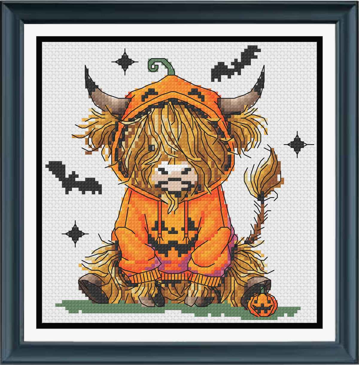 A framed cross-stitch of a fluffy Highland cow wearing an orange pumpkin costume, seated on a small patch of green grass with bats, stars, and a jack-o'-lantern around it. 