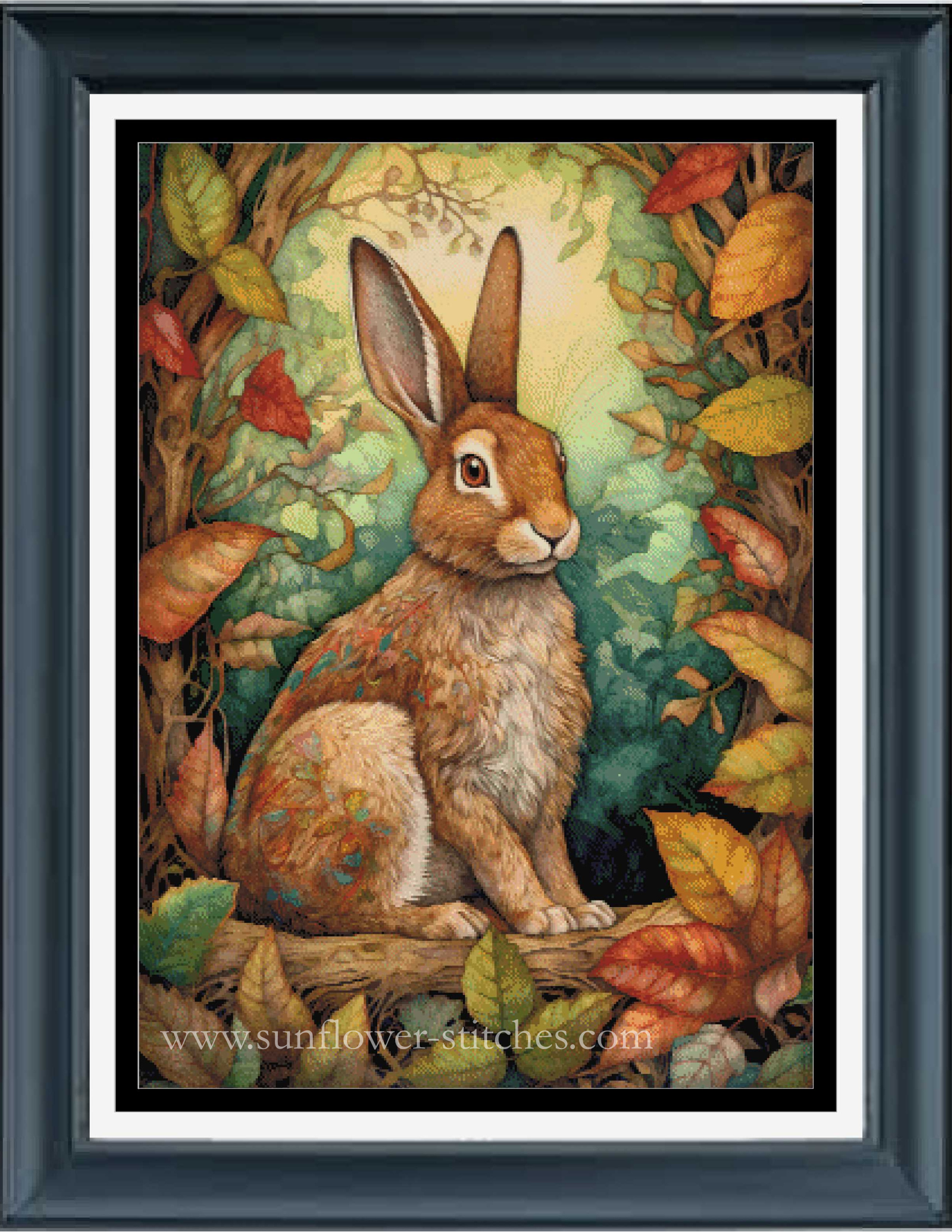Framed cross stitch featuring an illustration of a brown rabbit sitting on a log in a forest with autumn leaves.