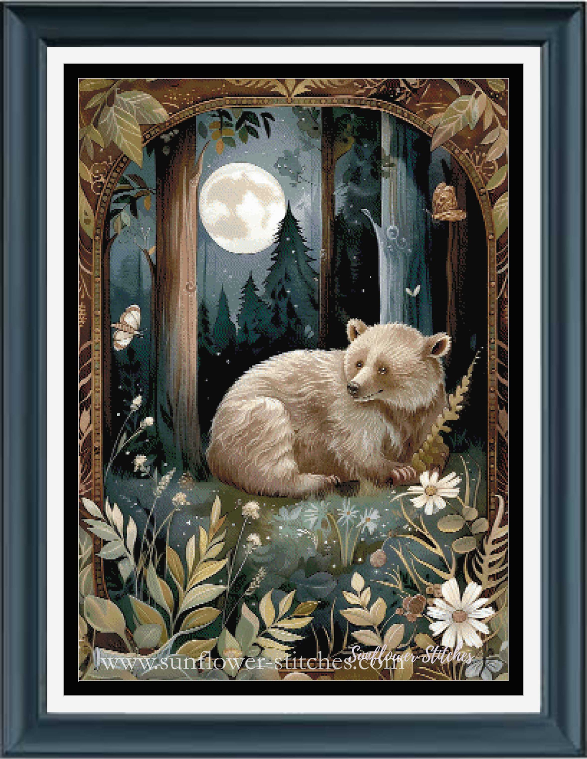 Framed cross stitch featuring a sleeping brown bear cub in a moonlit forest, surrounded by flowers and butterflies, with a dark blue frame and white mat.