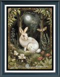 A framed cross stitch featuring a white rabbit sitting in a moonlit forest with flowers, foliage, a butterfly, and a decorative border. The artwork is presented in a dark blue frame with white matting.